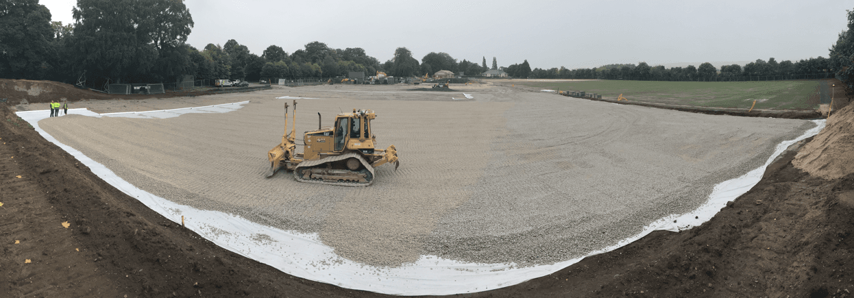 Tracked machine grading a pitch profile bordered by white material