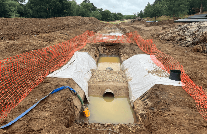 Open trench with pipework and protective fencing on the golf course