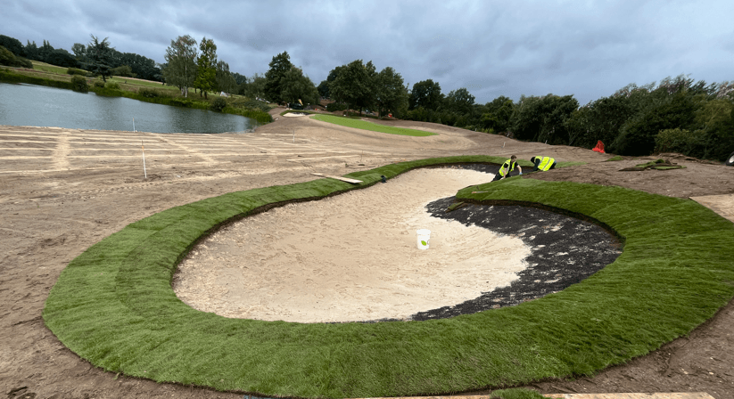 Sand-filled bunker beside a green and surrounding renovation works